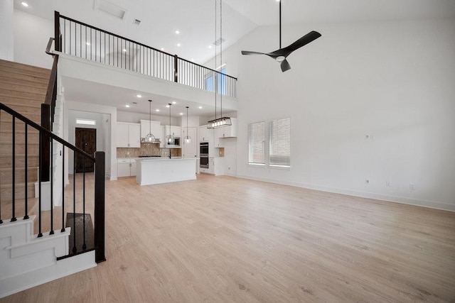 1601 Cardinal Ln, Round Rock, TX 78681 - unfurnished living room with ceiling fan, stairway, light wood finished floors, a towering ceiling, and baseboards