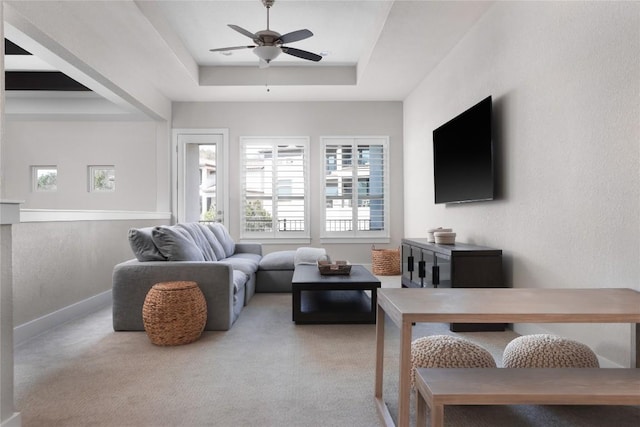 living room with a tray ceiling, carpet floors, baseboards, and ceiling fan