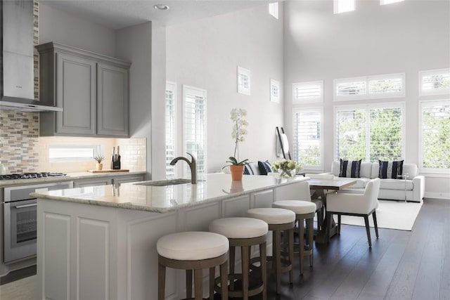 kitchen featuring a sink, decorative backsplash, stainless steel appliances, gray cabinetry, and wall chimney range hood