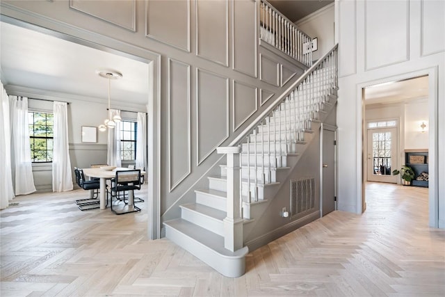 staircase with visible vents, a decorative wall, ornamental molding, a towering ceiling, and a notable chandelier