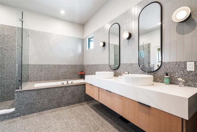 full bath featuring granite finish floor, tile walls, a garden tub, and a sink