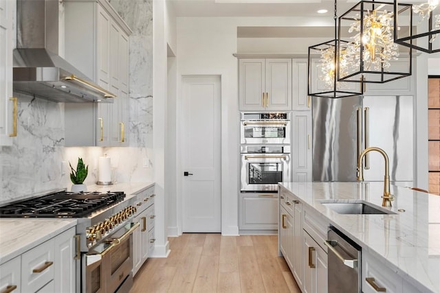 3113 Stableford Cv, Spicewood, TX 78669 - kitchen with appliances with stainless steel finishes, wall chimney exhaust hood, tasteful backsplash, light wood-type flooring, and a chandelier