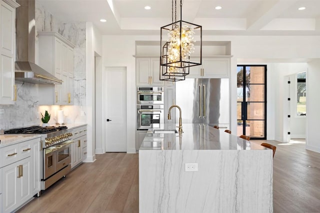 3113 Stableford Cv, Spicewood, TX 78669 - kitchen featuring premium appliances, wall chimney exhaust hood, backsplash, light wood-style flooring, and a chandelier