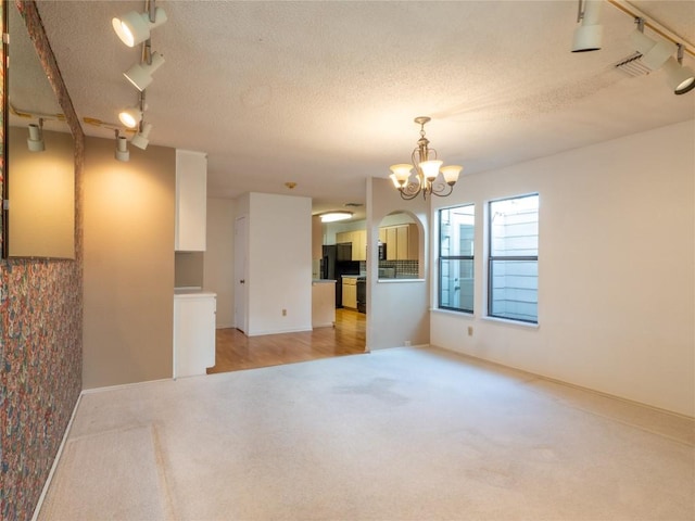 3379 S El Dorado, Lakeway, TX 78734 - unfurnished living room with track lighting, light carpet, arched walkways, a chandelier, and a textured ceiling