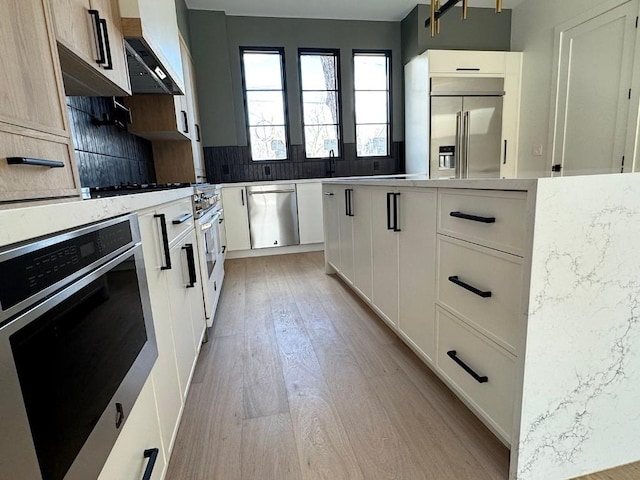705 E 50th St, Austin, TX 78751 - kitchen featuring wall chimney range hood, decorative backsplash, light wood-style flooring, stainless steel appliances, and white cabinetry