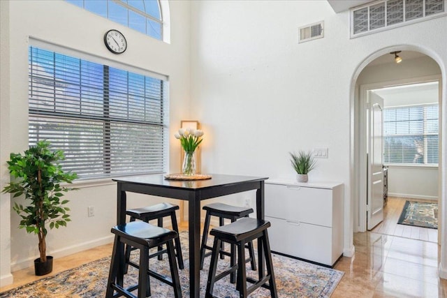 dining space featuring arched walkways, a towering ceiling, visible vents, and baseboards