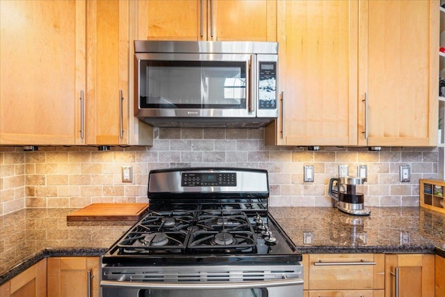 kitchen with appliances with stainless steel finishes, decorative backsplash, and dark stone countertops