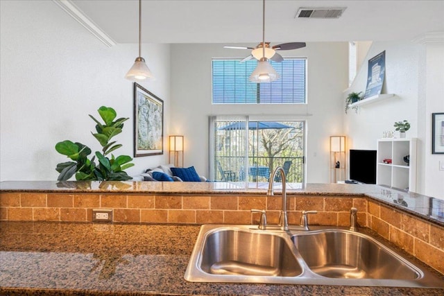 kitchen with brown cabinets, visible vents, a sink, dark stone counters, and hanging light fixtures