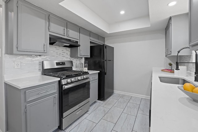 1002 Parkside Cir, Round Rock, TX 78664 - kitchen with stainless steel range with gas cooktop, under cabinet range hood, gray cabinets, a raised ceiling, and recessed lighting