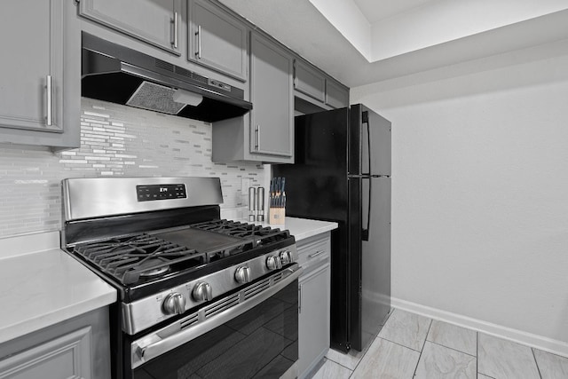1002 Parkside Cir, Round Rock, TX 78664 - kitchen featuring gas stove, under cabinet range hood, gray cabinetry, tasteful backsplash, and freestanding refrigerator
