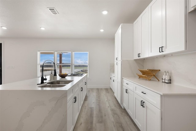 195 Bianca Cir, Del Valle, TX 78617 - kitchen with light wood-style flooring, white cabinetry, recessed lighting, a center island with sink, and light stone countertops