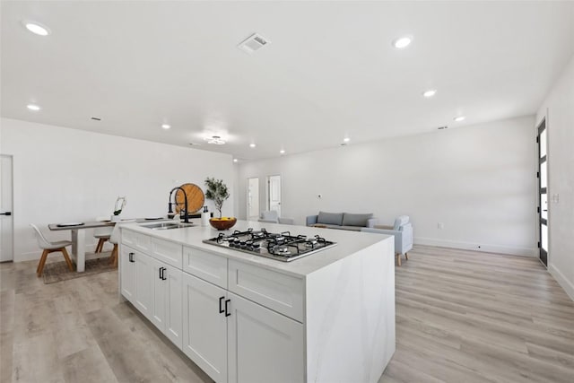 195 Bianca Cir, Del Valle, TX 78617 - kitchen with stainless steel gas cooktop, light wood-style floors, recessed lighting, white cabinetry, and a kitchen island with sink