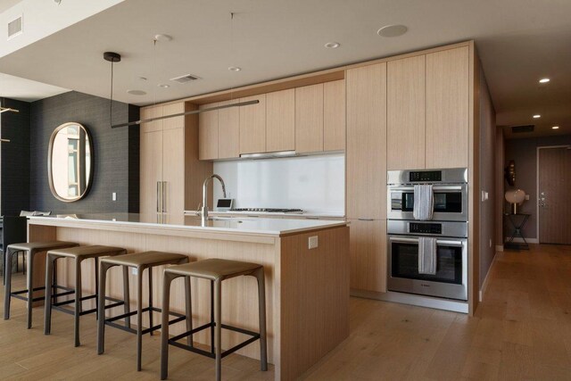 44 E Ave Unit 2601, Austin, TX 78701 - kitchen with stainless steel double oven, modern cabinets, light brown cabinets, a kitchen island with sink, and light wood-style floors