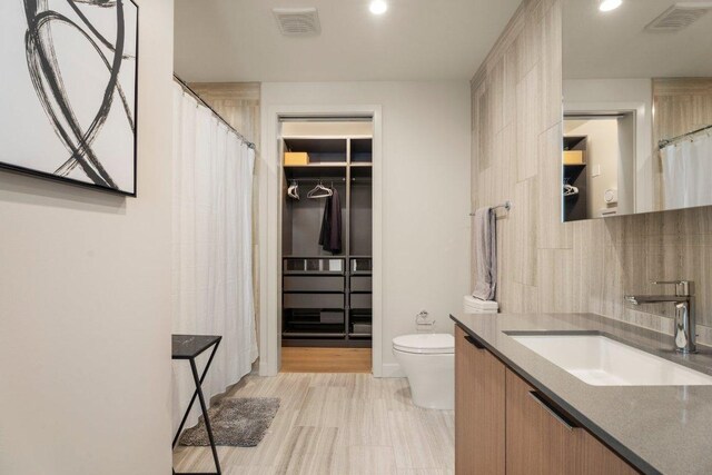 44 E Ave Unit 2601, Austin, TX 78701 - bathroom with toilet, decorative backsplash, vanity, curtained shower, and a walk in closet