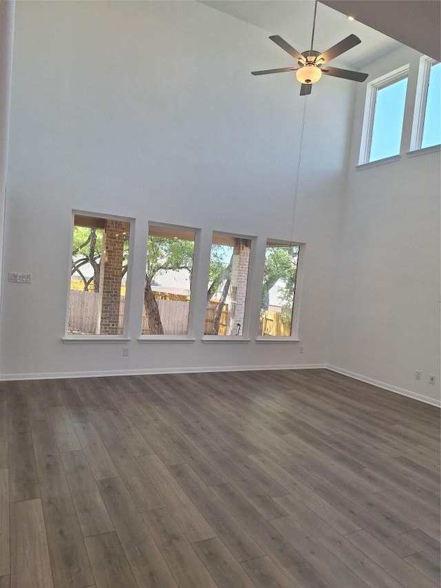 unfurnished living room featuring dark wood-type flooring, a towering ceiling, and a healthy amount of sunlight