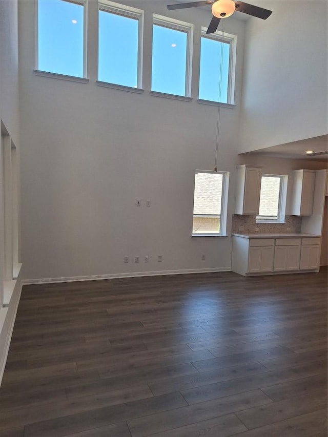 unfurnished living room featuring dark wood-style floors, a high ceiling, baseboards, and ceiling fan