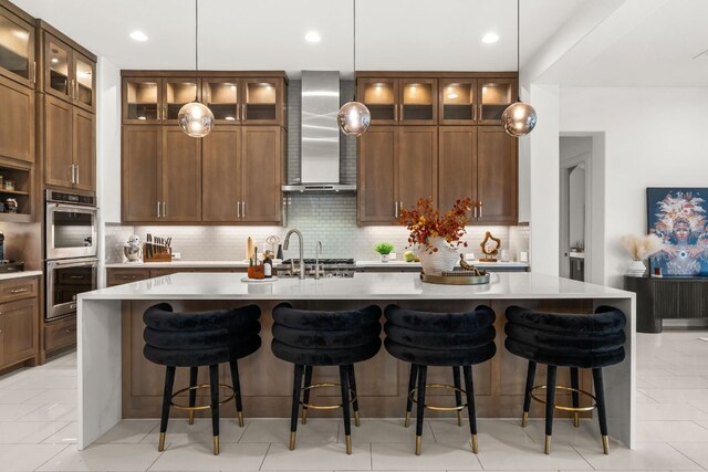 702 Serene Estates Dr, Austin, TX 78738 - kitchen featuring wall chimney exhaust hood, stainless steel double oven, a kitchen island with sink, decorative backsplash, and light countertops