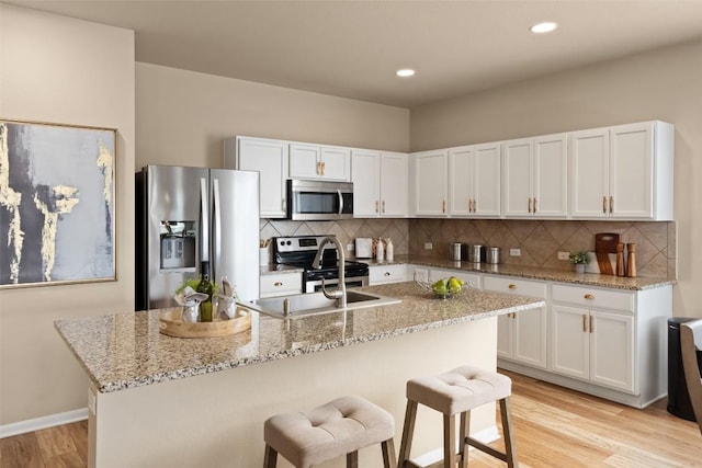 122 Denton Dr, Hutto, TX 78634 - kitchen with a kitchen bar, stainless steel appliances, white cabinets, light wood finished floors, and light stone countertops