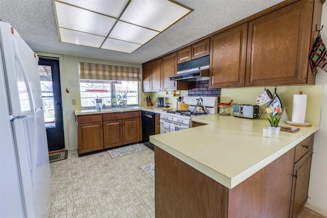 kitchen with brown cabinets, under cabinet range hood, light countertops, white appliances, and a peninsula