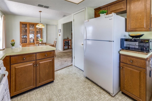 kitchen featuring visible vents, light countertops, freestanding refrigerator, and brown cabinets