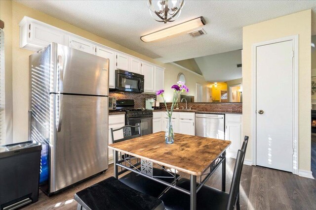 14300 Anita Marie Ln, Austin, TX 78728 - kitchen with black appliances, dark countertops, white cabinets, dark wood finished floors, and vaulted ceiling