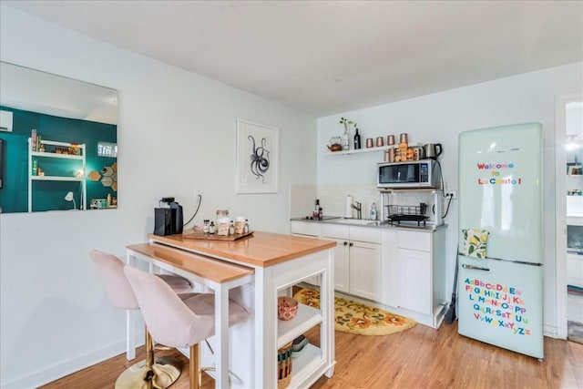 203 Ben Howell Dr, Austin, TX 78704 - kitchen with stainless steel microwave, freestanding refrigerator, white cabinetry, light wood finished floors, and light countertops
