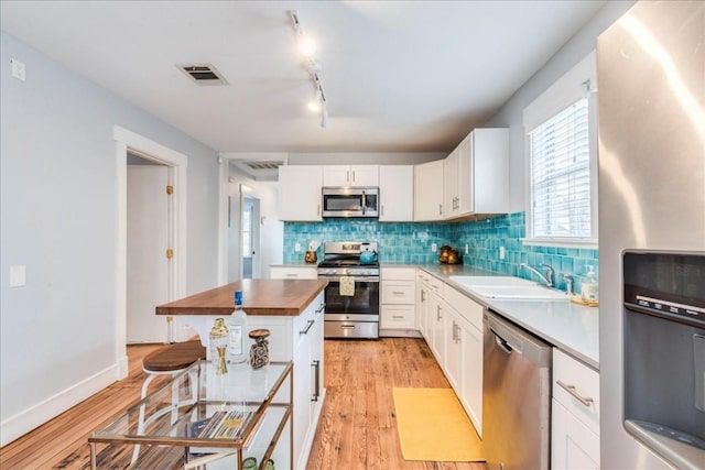 203 Ben Howell Dr, Austin, TX 78704 - kitchen with stainless steel appliances, butcher block counters, light wood-type flooring, tasteful backsplash, and white cabinetry