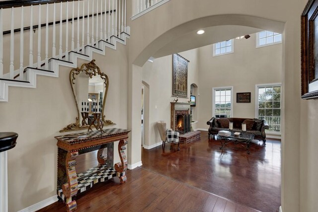 interior space featuring a fireplace, a high ceiling, baseboards, arched walkways, and hardwood / wood-style floors