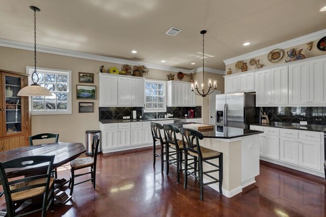 kitchen with a chandelier, a center island, dark countertops, stainless steel refrigerator with ice dispenser, and visible vents