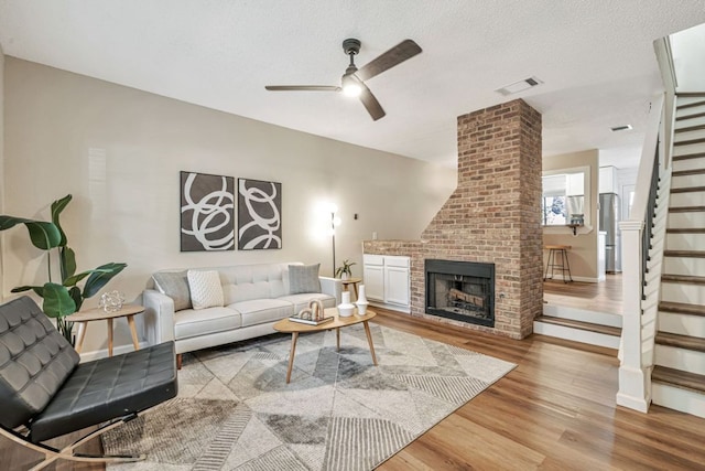 living room with visible vents, wood finished floors, a fireplace, ceiling fan, and stairway