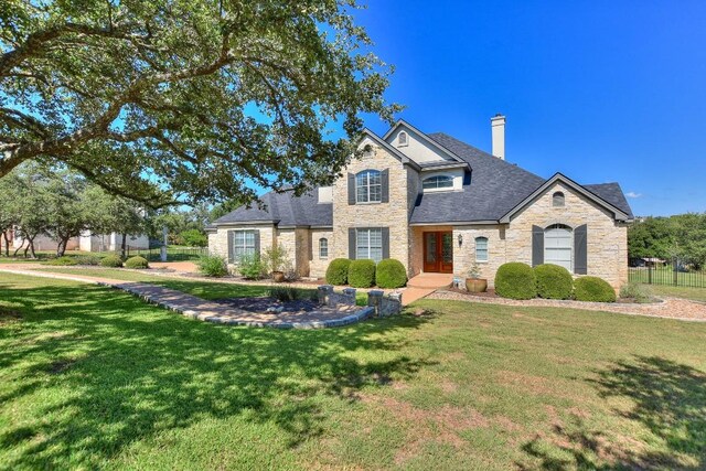 traditional-style house featuring a chimney, fence, stone siding, french doors, and a front lawn