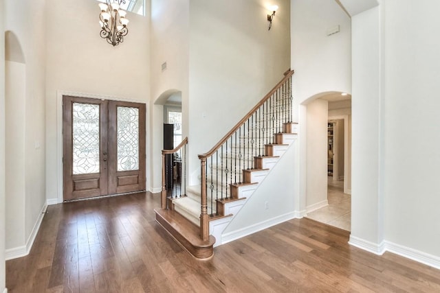 foyer entrance with arched walkways, baseboards, wood finished floors, a high ceiling, and stairway