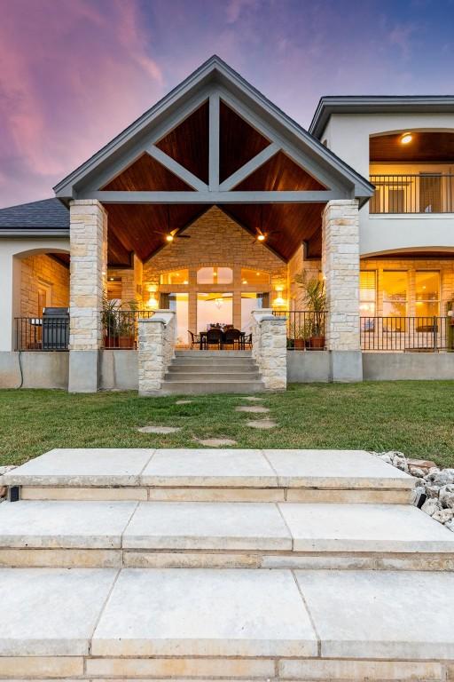 exterior entry at dusk with stone siding, a porch, and stucco siding