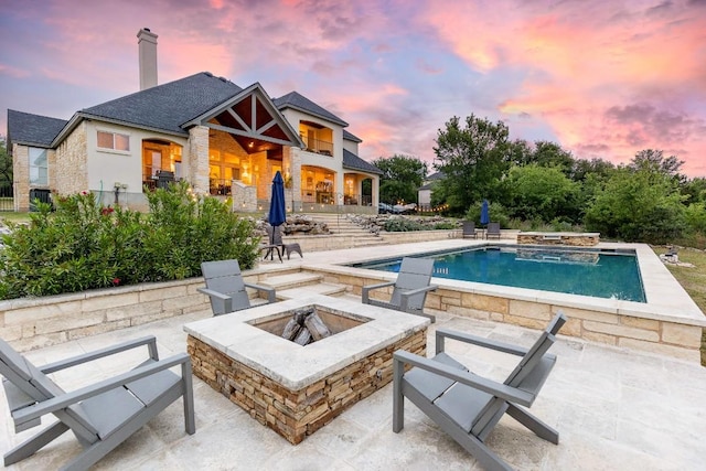pool at dusk with a patio, a fire pit, and an outdoor pool