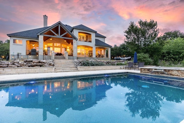 pool at dusk with stairway, a patio area, and an outdoor pool