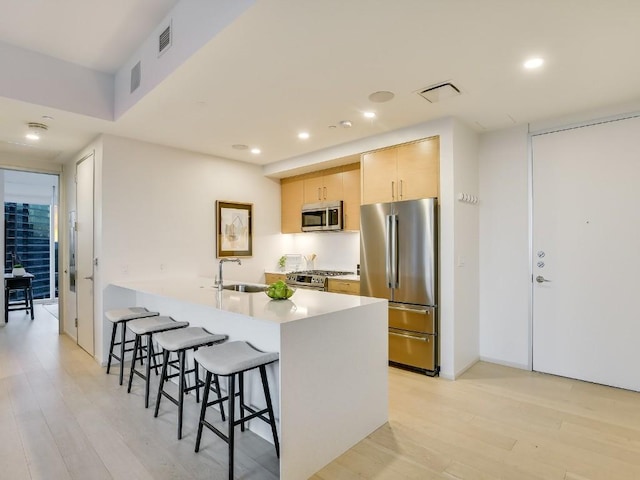 301 W Ave Unit 1301, Austin, TX 78701 - kitchen with appliances with stainless steel finishes, a sink, a kitchen bar, light brown cabinets, and light wood finished floors