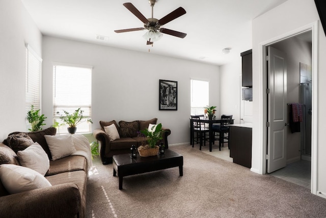 living area with visible vents, light colored carpet, baseboards, and a ceiling fan
