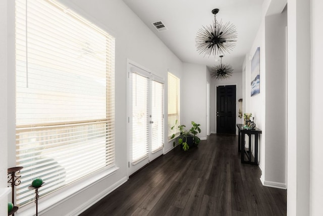 hall with dark wood finished floors, visible vents, an inviting chandelier, and baseboards