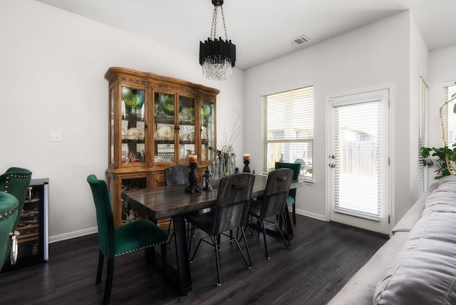 dining area with dark wood finished floors, a notable chandelier, visible vents, and baseboards