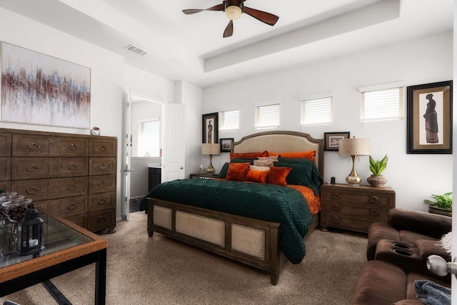 bedroom featuring a tray ceiling, light carpet, multiple windows, and visible vents
