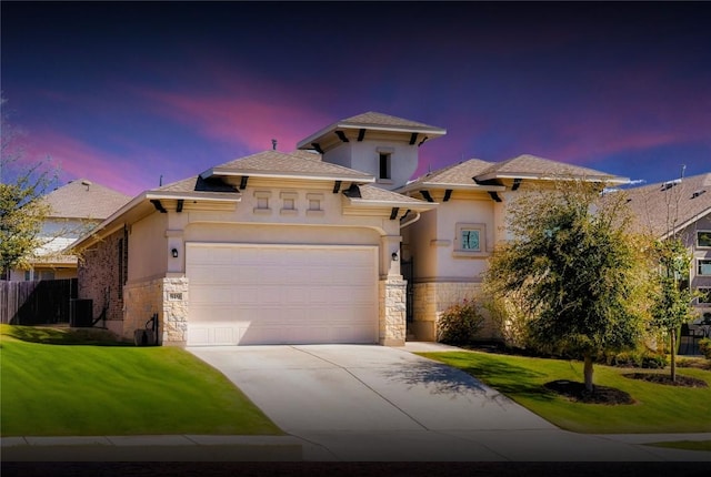 view of front of property with stucco siding, stone siding, central AC, a yard, and concrete driveway