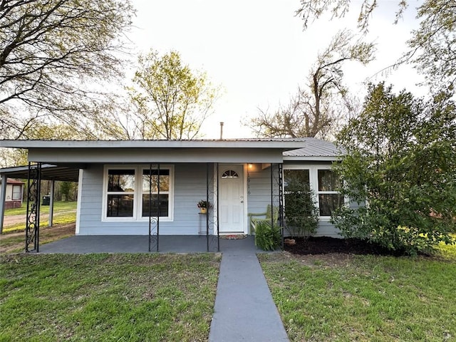 view of front of property featuring metal roof, a front lawn, a carport, and covered porch