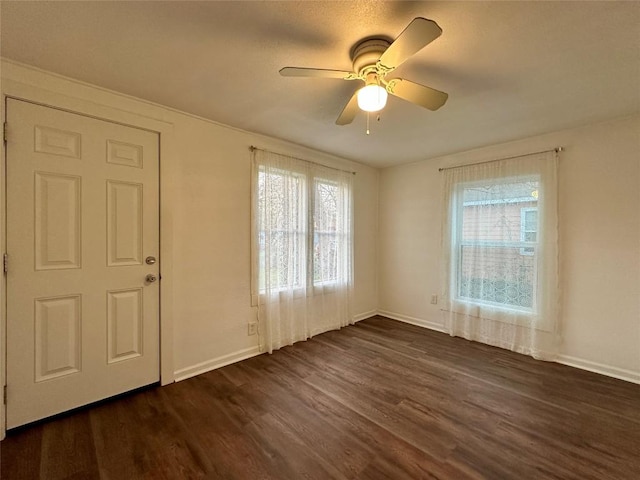 spare room featuring a ceiling fan, dark wood-style flooring, and baseboards