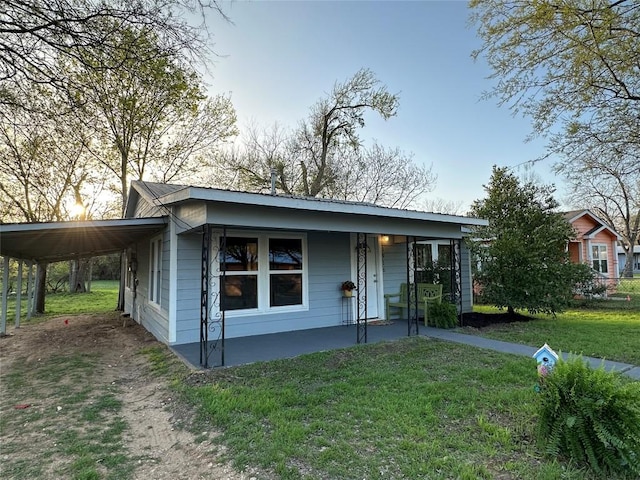 view of front of home with covered porch, dirt driveway, a carport, and a front yard