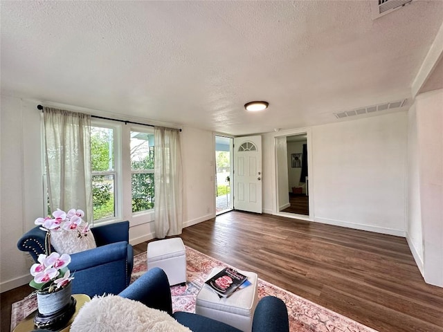 living room featuring a textured ceiling, visible vents, wood finished floors, and baseboards