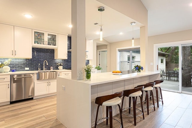 8702 Silverhill Ln, Austin, TX 78759 - kitchen featuring stainless steel dishwasher, a sink, light wood-style floors, a breakfast bar, and decorative backsplash