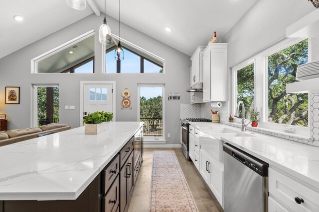 631 Lakeside Dr, Wimberley, TX 78676 - kitchen with lofted ceiling with beams, appliances with stainless steel finishes, white cabinets, decorative backsplash, and light stone countertops