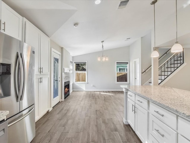 10310 Bilbrook Pl, Austin, TX 78748 - kitchen with stainless steel fridge with ice dispenser, lofted ceiling, a lit fireplace, white cabinetry, and light wood-style flooring