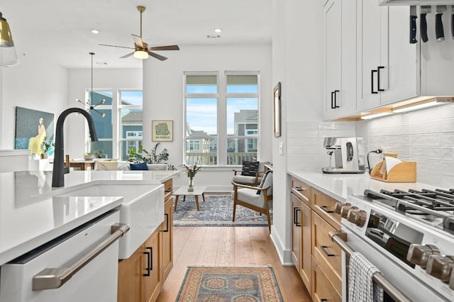 kitchen featuring gas range, light wood-style floors, light countertops, white dishwasher, and ceiling fan