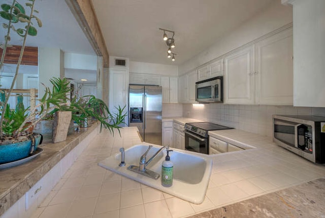 614 Sunfish St, Lakeway, TX 78734 - kitchen featuring appliances with stainless steel finishes, white cabinets, backsplash, and tile countertops